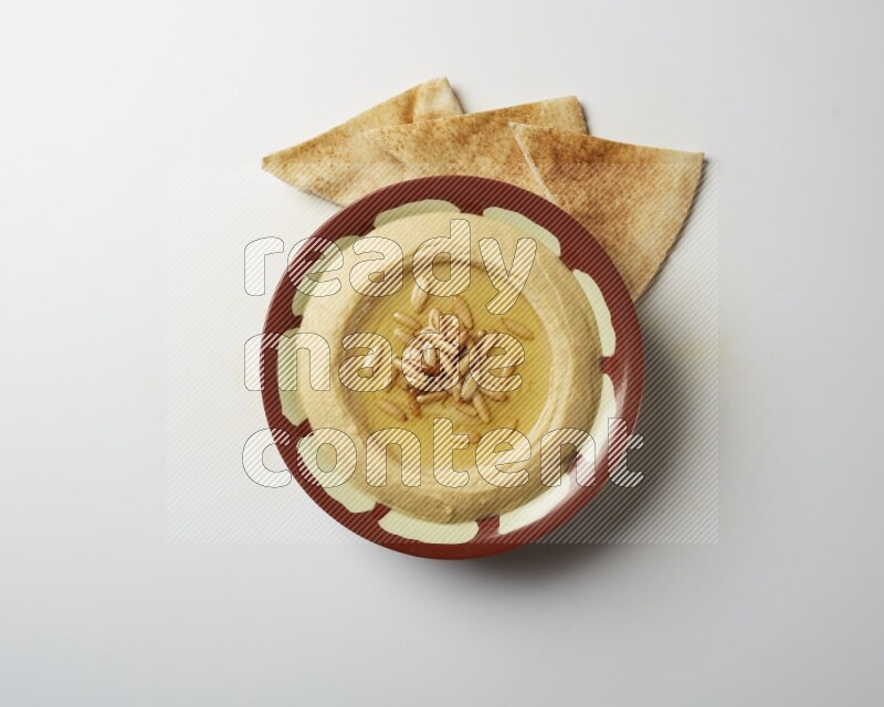 Hummus in a traditional plate garnished with pine nuts on a white background