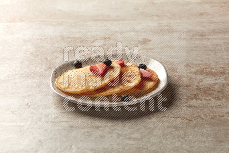 Three stacked mixed berries pancakes in an irregular plate on beige background