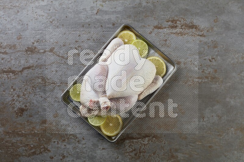whole Raw chicken on a small oven trey direct on a rustic grey background