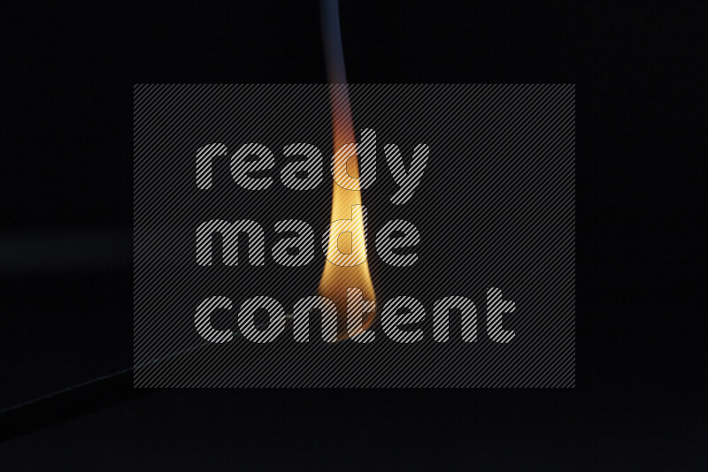 A burning incense stick isolated on dark backdrop