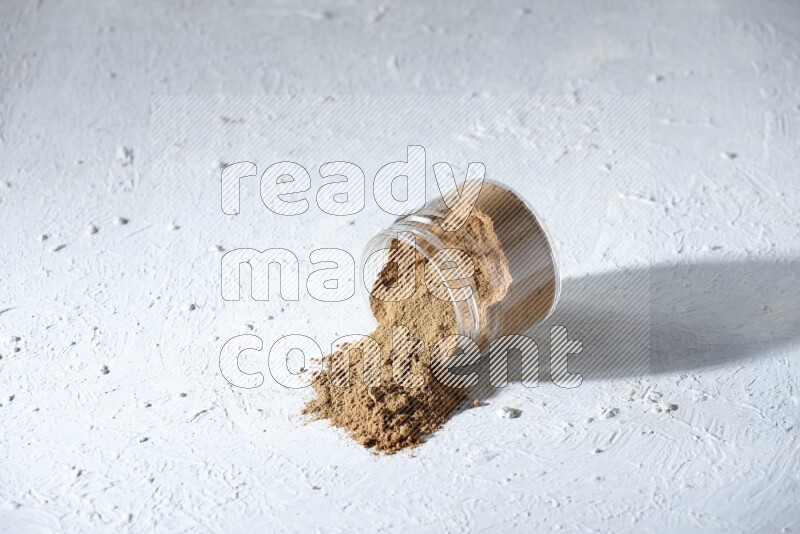 A flipped glass jar full of allspice powder and powder spilled out of it on a textured white flooring