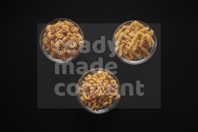 Different pasta types in glass bowls on black background