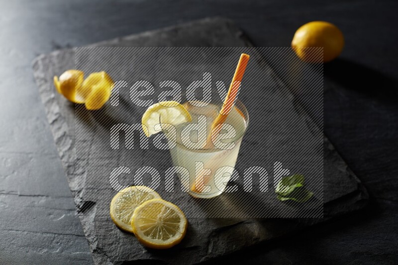 A glass of lemon juice with a straw on black background