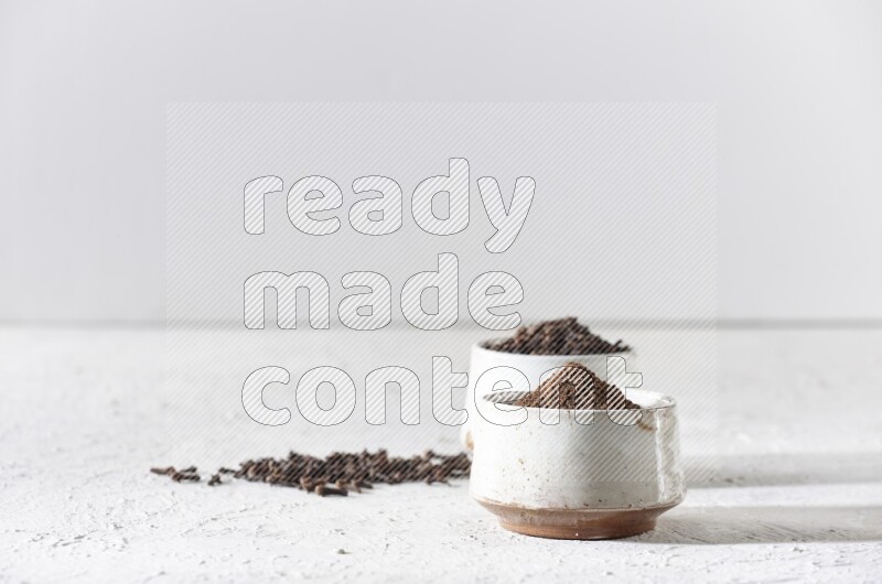 2 Beige ceramic bowls, one full of cloves and the other full of powder on textured white flooring