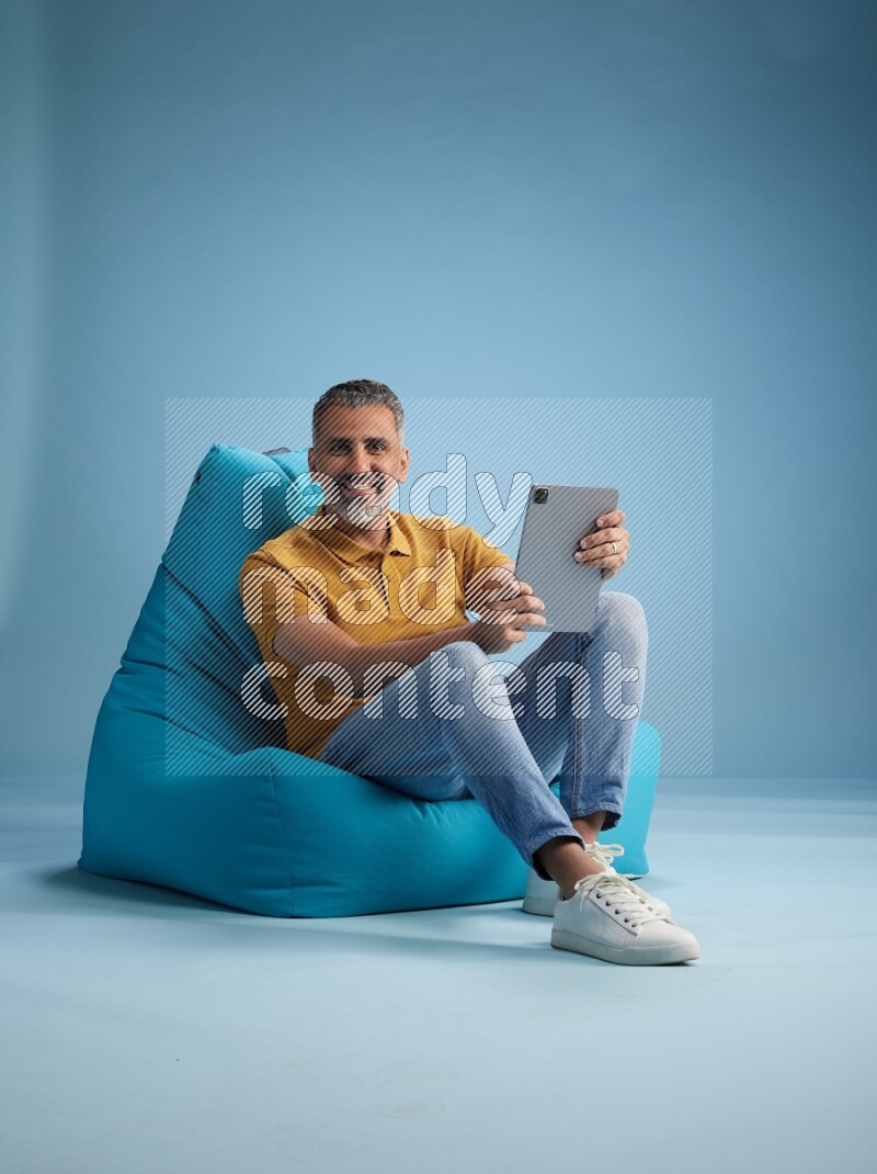 A man sitting on a blue beanbag and working on tablet