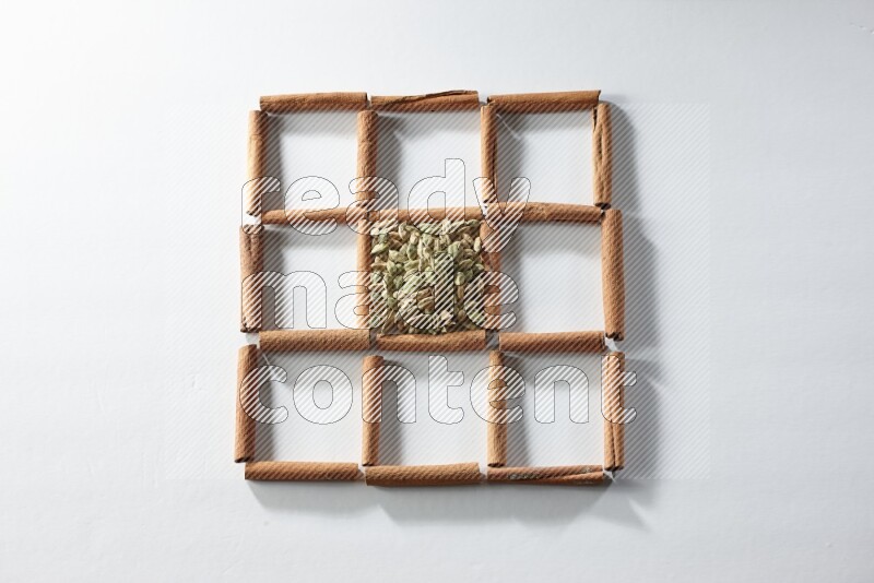 9 squares of cinnamon sticks full of cardamom in the middle surrounded by nutmeg, cinnamon, bay laurel leaves, cloves, cumin, dried ginger, dried basil and star anise on white flooring