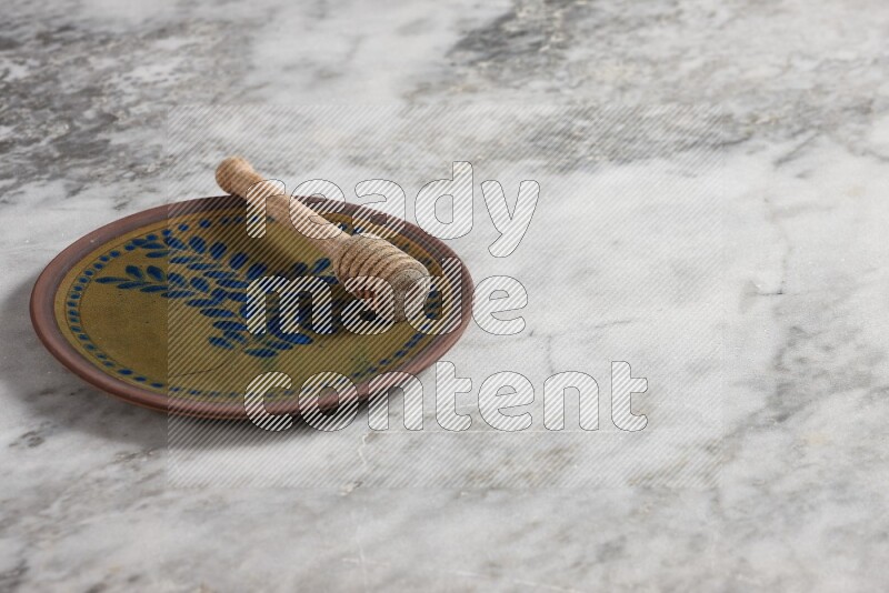 Decorative pottery plate with wooden honey dipper in it on grey marble background