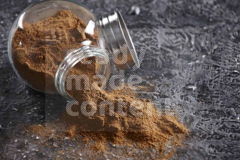 Flipped herbal glass jar full of cinnamon powder on textured black background