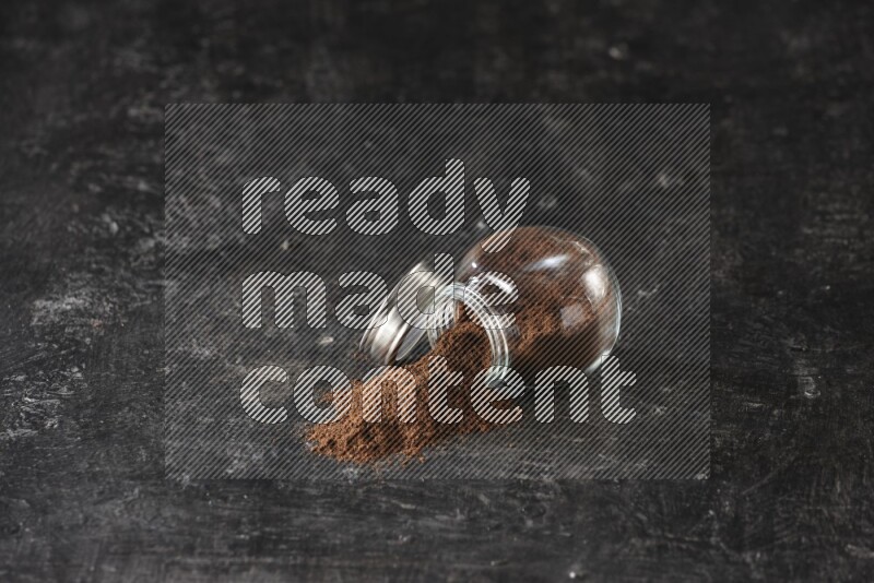 وعاء زجاجي للتوابل مقلوب ممتلئ ببودرة القرنفل والبودرة سقطت منه على أرضية سوداء