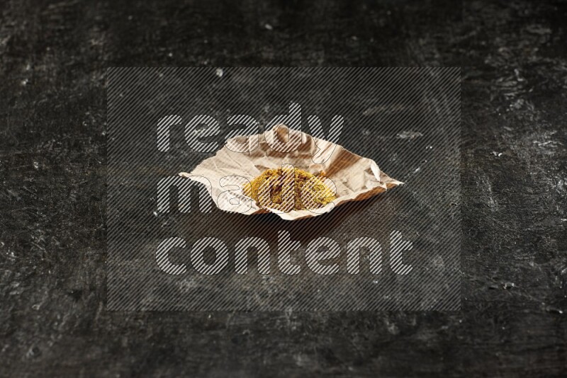 Turmeric powder in a crumpled piece of paper on textured black flooring