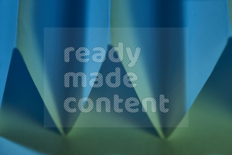 A close-up abstract image showing sharp geometric paper folds in green and blue gradients