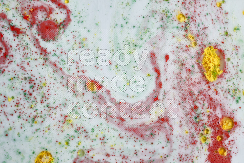 The image captures a splatter of yellow, red and green paint over a white backdrop