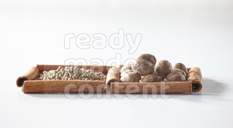 2 squares of cinnamon sticks full of white pepper and nutmegs on white flooring