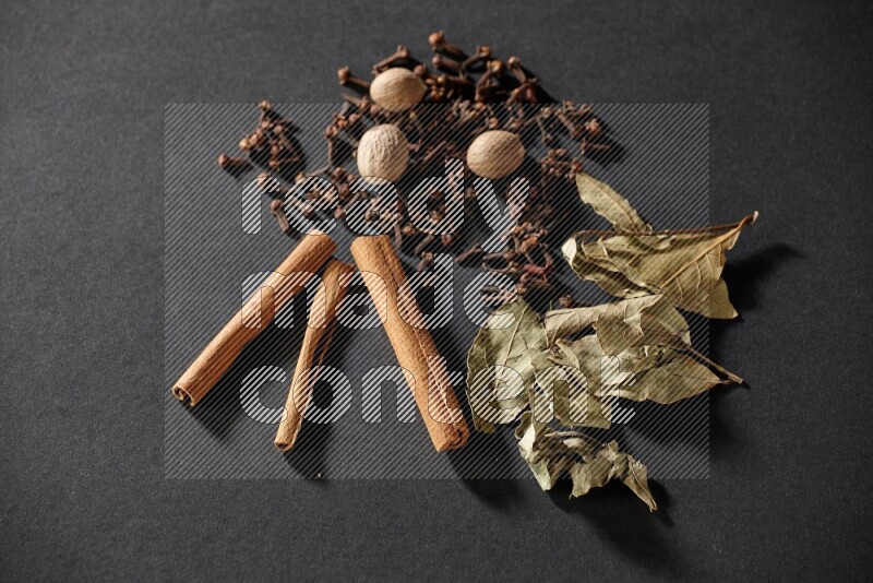 Cloves, ginger, bay laurel and cinnamon sticks on black flooring