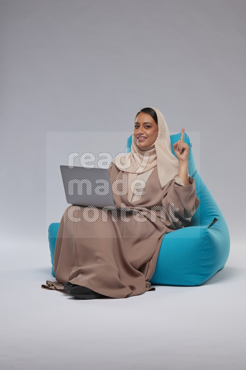 A Saudi woman sitting on a blue beanbag and working on laptop