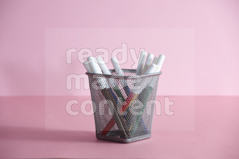 Pens, pencils and other different school supplies in a metal pen holder on rose background