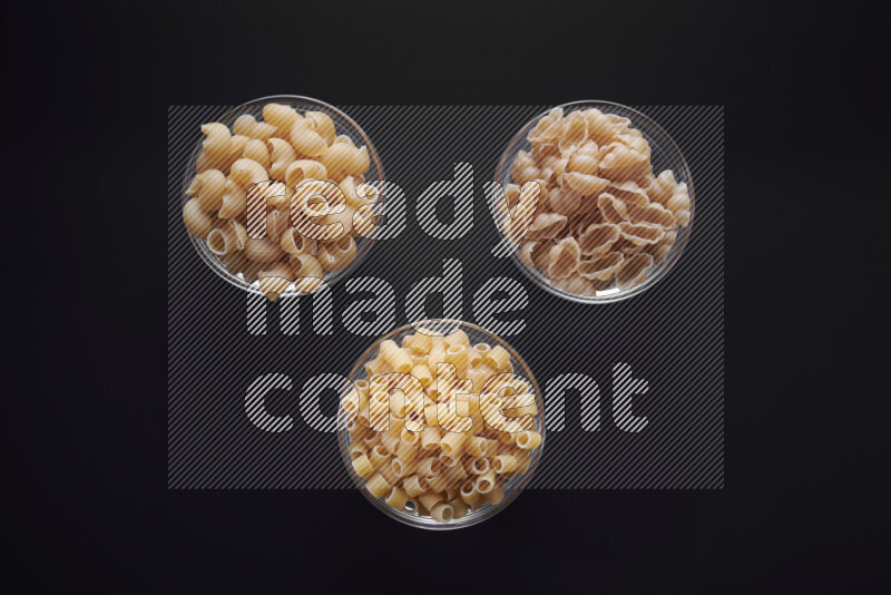 Different pasta types in glass bowls on black background