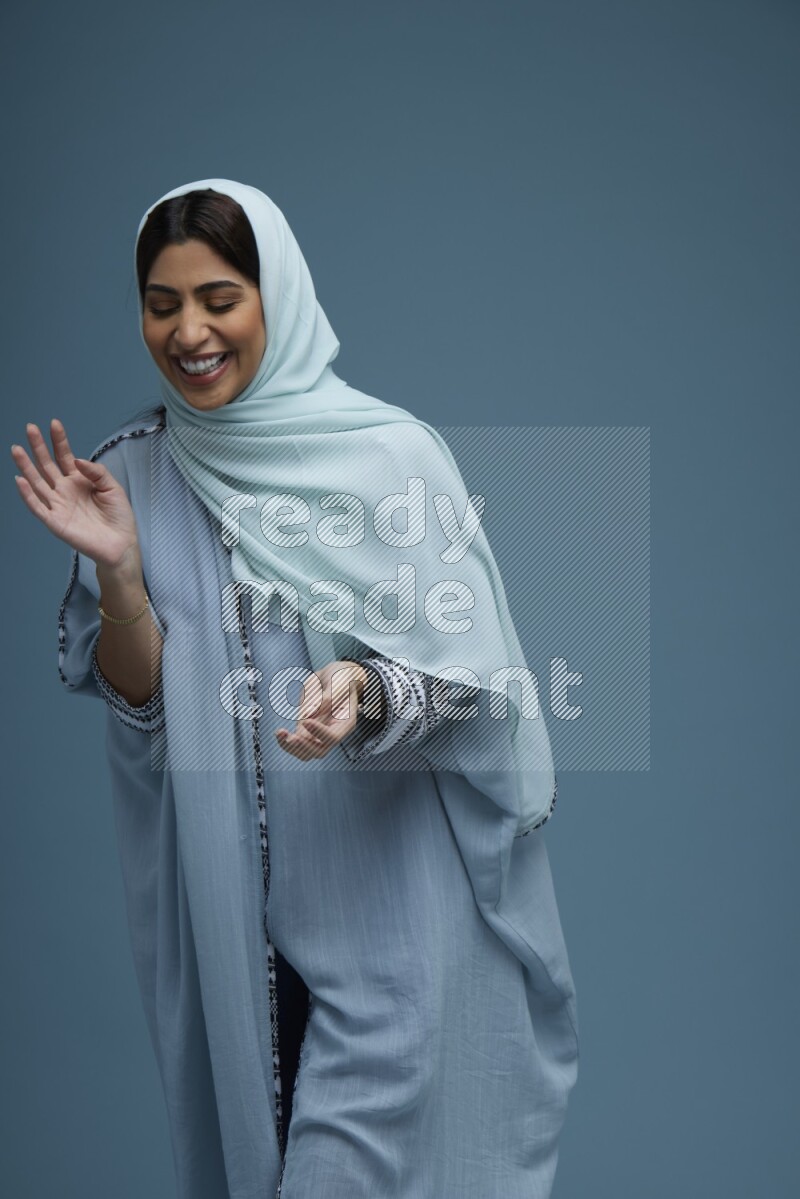 A woman posing in a blue background wearing a blue Abaya with hijab