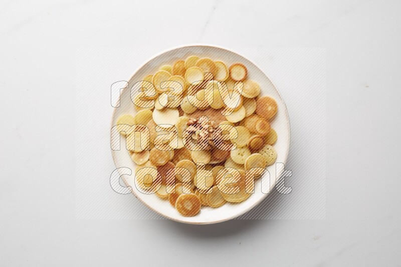 Top-view shot of walnut cereal pancakes in a round bowl on white background