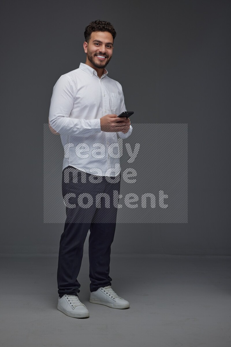 A man wearing smart casual standing and using his phone eye level on a gray background