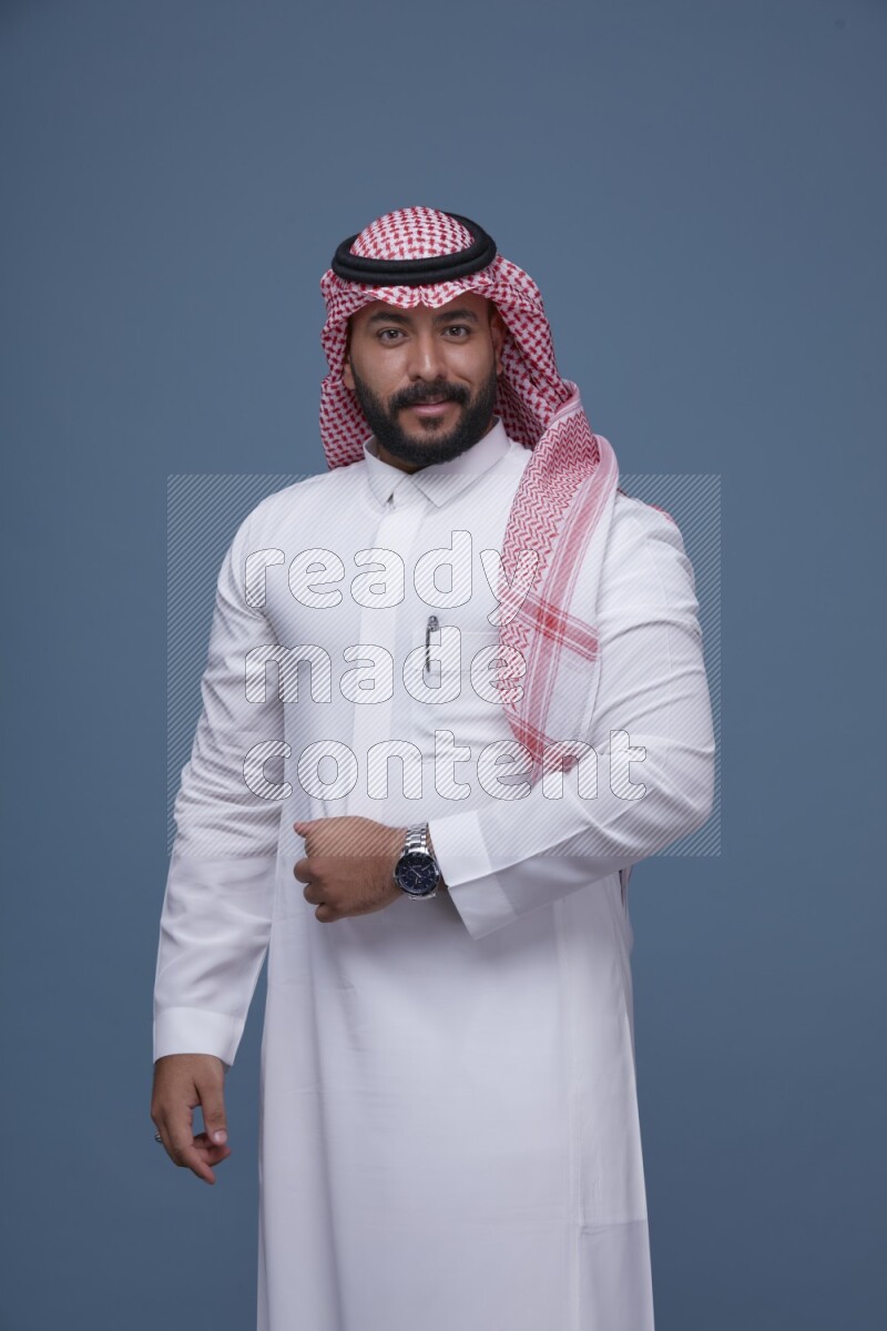 A Saudi man posing on blue background wearing Thob and Shomag